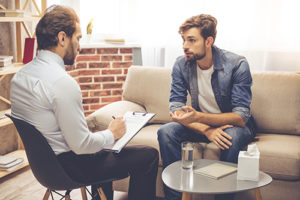 male patient sits on couch and talks to counselor with clipboard in morphine addiction treatment