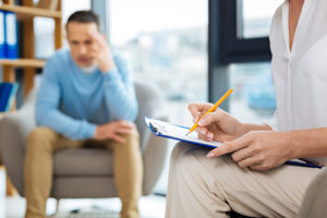 man sits in a chair talking to a counselor in oxycodone addiction treatment