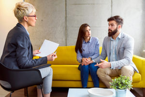 a couple sits on a couch talking to a female counselor in relationship therapy