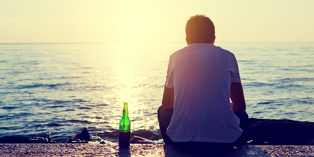 a man with a beer bottle looking out on the water asking himself can alcohol cause depression