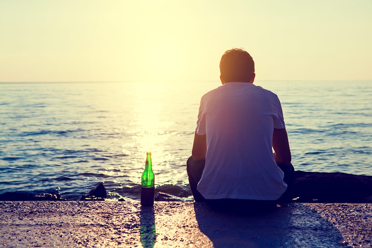a man with a beer bottle looking out on the water asking himself can alcohol cause depression